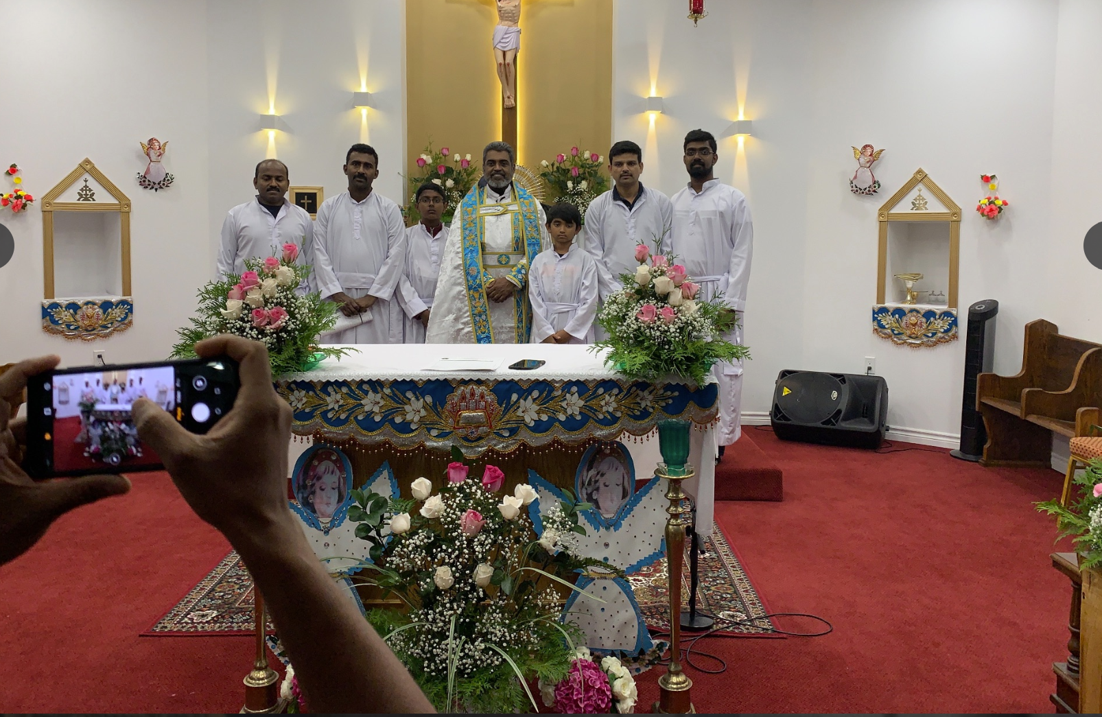 Group photo of clergy and congregation members around ornately decorated altar with flowers